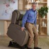 An older man uses the EZ Sleeper with Twilight Lift Chair to stand up in a living room featuring light wood shelves, a plant, and artwork in the background.