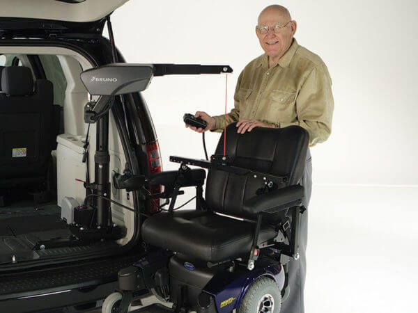 Older gentleman holding remote for Big Lifter in back of van attached to power wheelchair