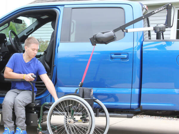 Young man sitting in transfer seat looking at wheelchair attached to Out Rider lift in back bed of truck
