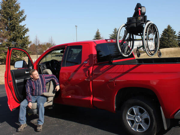man in turning seat in red pickup truck with out-rider hoist lift in back of truck bed