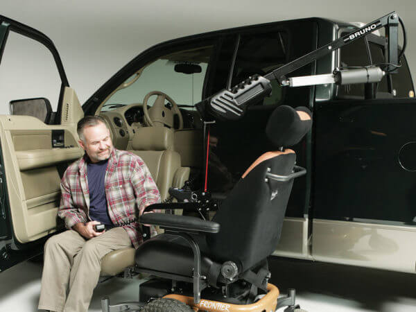 Man in turn-out transfer seat looking at power chair attached to Out Rider lift in back of pickup truck
