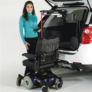 Woman standing next to power wheelchair using bruno lift on back of white vehicle