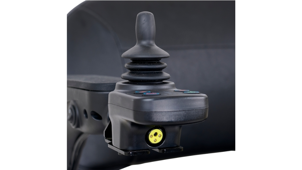 Close-up of a black joystick controller with buttons and a yellow connector port, attached to the Buzzaround CarryOn Power Wheelchair.