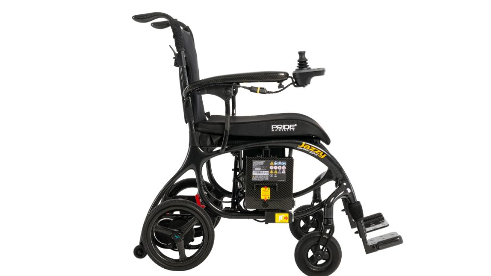 Jazzy Carbon 27X Power Wheelchair in black, featuring joystick control, a visible battery pack under the seat, and footrests; photographed against a white background.