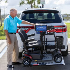 An older man in a blue shirt loads a mobility scooter onto a Harmar Universal Scooter Lift (AL100) attached to the back of an SUV in a parking lot.