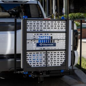A Harmar Extra Large Fusion Lift (AL301XL) is mounted on the back of a white vehicle, featuring a metal platform with a star pattern design for transporting large scooters.