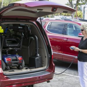 A woman uses a remote control to operate a Harmar Premium Inside Lift (AL435), loading a mobility scooter into the back of a red SUV in a parking lot.