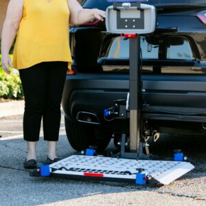 A person stands next to a black car with a Harmar Universal Powerchair Lift (AL500) attached to the vehicle’s rear hitch.