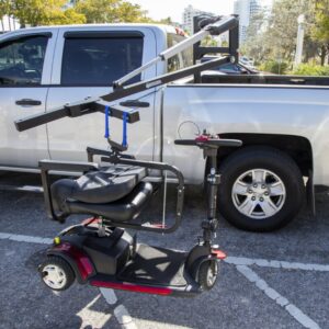 The Harmar 150 Speed Crew Cab Lift (AL815CC) is lifting a mobility scooter into the bed of a silver pickup truck in a parking lot.
