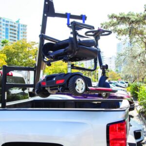 A Harmar 150 Speed Crew Cab Lift (AL815CC) is being used to lift a mobility scooter into the bed of a white pickup truck in a sunny urban area.
