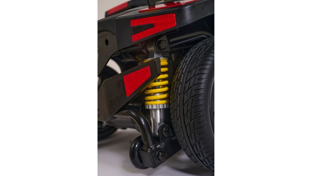 Close-up of a yellow coil spring suspension and tire on a black vehicle, featuring red reflective accents—ideal for upgrading both the performance and style of your Buzzaround XL+ 4-Wheel Scooter.