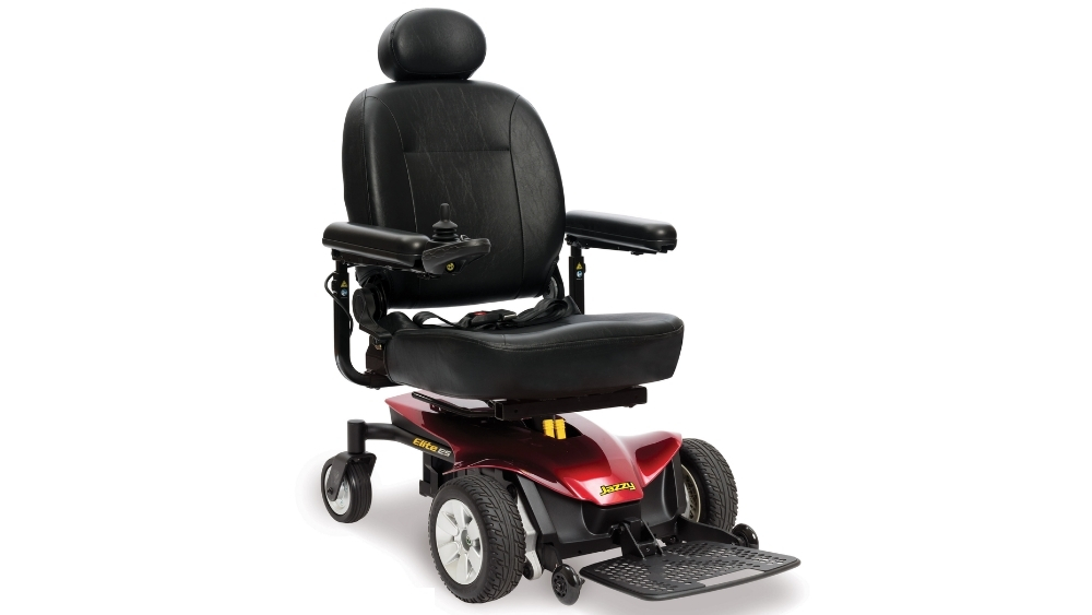 Experience comfortable and reliable mobility with the Jazzy Elite ES Power Wheelchair, featuring a black cushioned seat, supportive armrests, intuitive joystick control on the right armrest, and a vibrant red base with four wheels and a sturdy footrest platform.