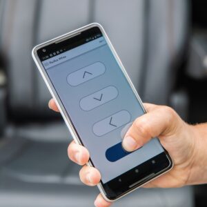 A hand holds a smartphone with an app controlling the BraunAbility Turny Evo, showing four large directional buttons—up, down, left, and a highlighted right button.