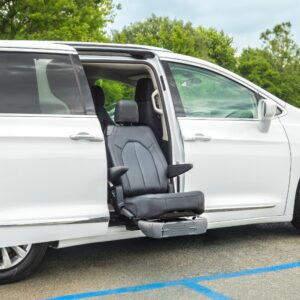 A white minivan is parked in a handicap spot with a BraunAbility Turny Evo front passenger seat extended outward for accessible entry and exit.