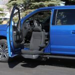 A blue pickup truck with its driver’s door open features the BraunAbility Turny Evo, which rotates and extends the driver’s seat outward for enhanced accessibility.