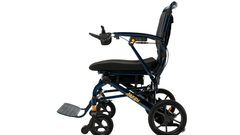 Side view of the Jazzy Carbon Travel Power Wheelchair, a compact and lightweight model featuring a joystick control on the right armrest, footrest, black seat, and sturdy wheels.