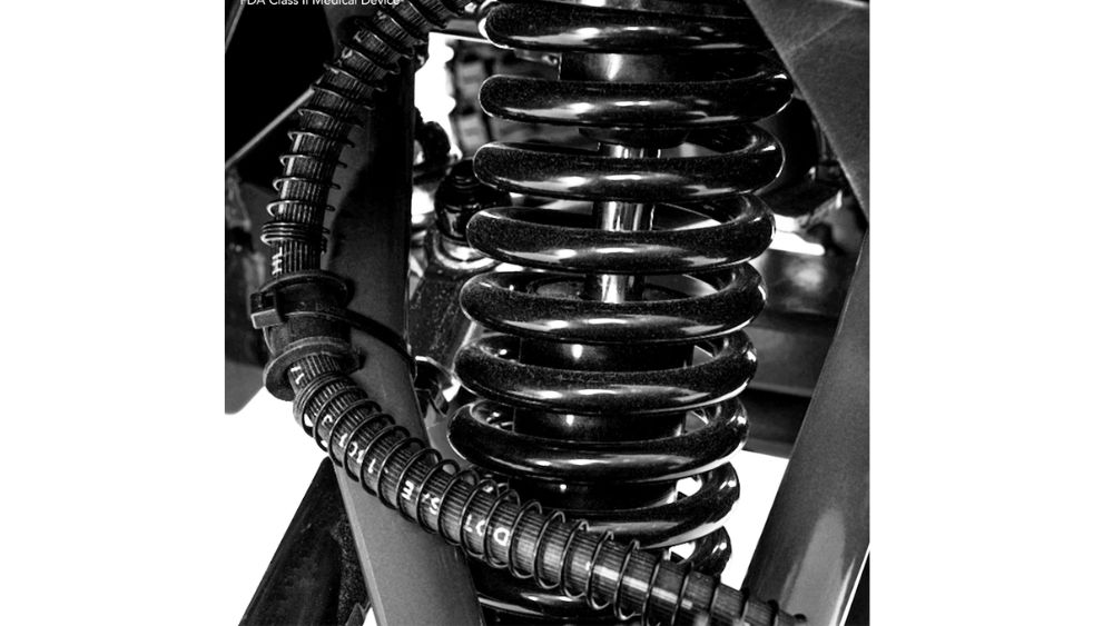 Close-up view of a coiled metal suspension spring and attached cable conduit, part of the Baja™ Wrangler® 2 4-Wheel Scooter’s outdoor suspension system.