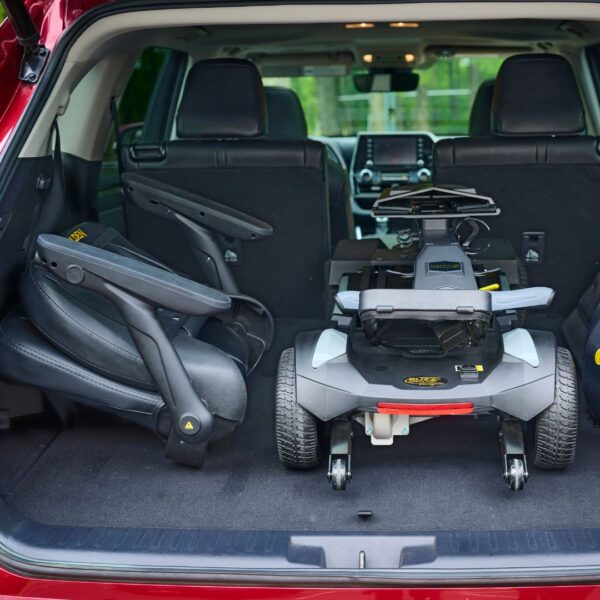 A Buzzaround CarryOn HD 4-Wheel Scooter and two folded child car seats are placed in the cargo area of an SUV with the rear door open.