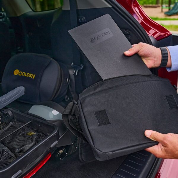 A person places a black Buzzaround CarryOn HD 4-Wheel Scooter into a black bag next to mobility equipment in the trunk of a red vehicle.