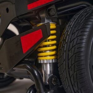 Close-up view of the Buzzaround XL+ 4-Wheel Scooter, highlighting its yellow coil spring suspension, tire, detailed mechanical components, and red reflectors.