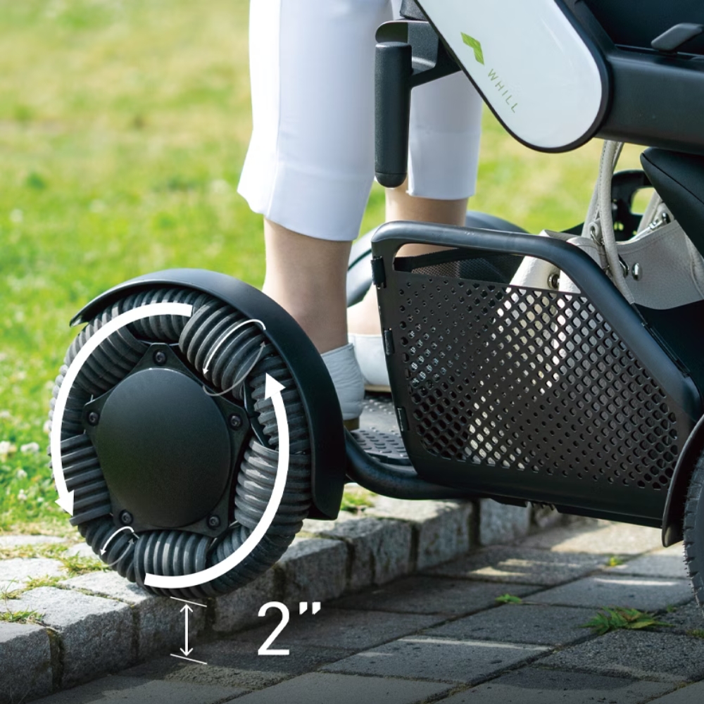 Using the WHILL Model C2 High Back electric wheelchair, an individual navigates a 2-inch curb onto grass with ease, showcasing the advanced climbing ability of its innovative wheels.
