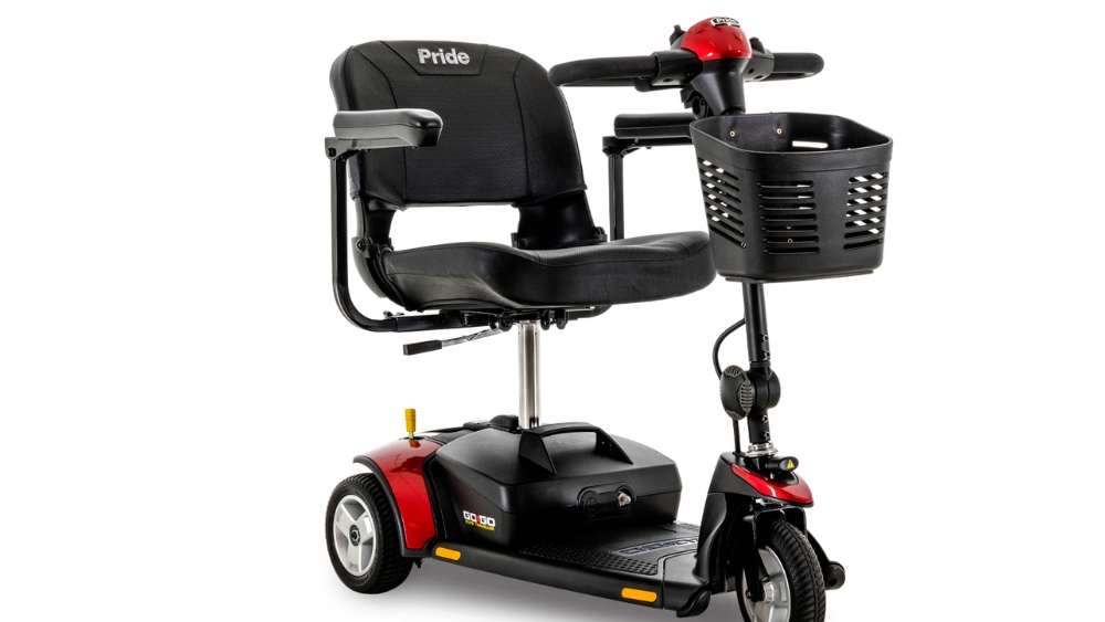 The Go Go Elite Traveller 3-Wheel Scooter is a mobility scooter with three wheels, equipped with a black seat, armrests, front basket, and bold red accents. The Pride brand name appears on the back of the seat.