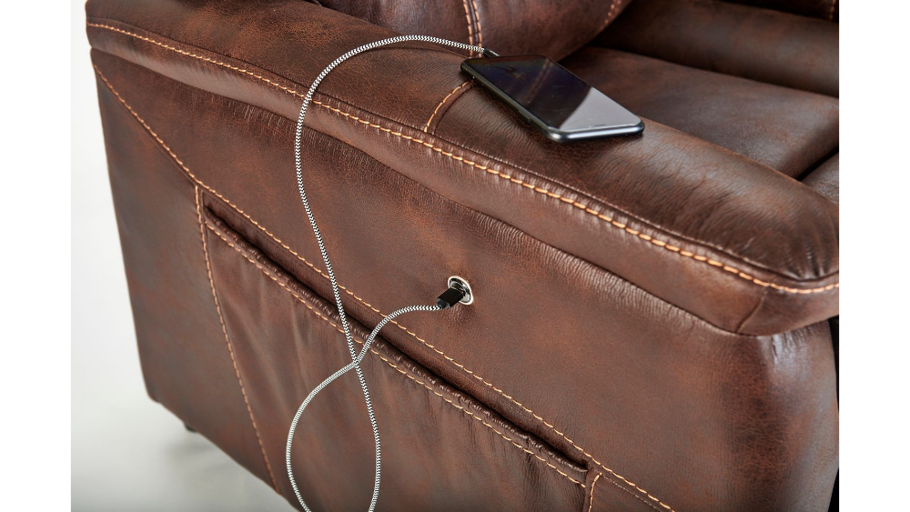 A smartphone charges through a cable connected to the USB port located on the armrest of the Dione Lift Chair.