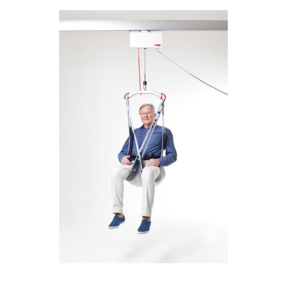 An older adult uses the Evo Hygiene Lowback ceiling-mounted patient lift, suspended in a harness against a plain white background.