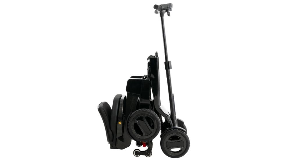 A Go Go™ Carbon 4-Wheel Scooter in black, shown fully collapsed and upright, displaying its wheels and handle.
