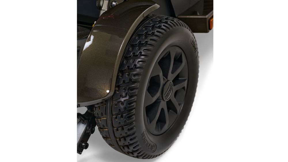 Close-up view of a black off-road tire with a rugged tread pattern mounted on a vehicle, showing part of the wheel arch and suspension, evoking the durability and stability of the Companion HD 3-Wheel Scooter.