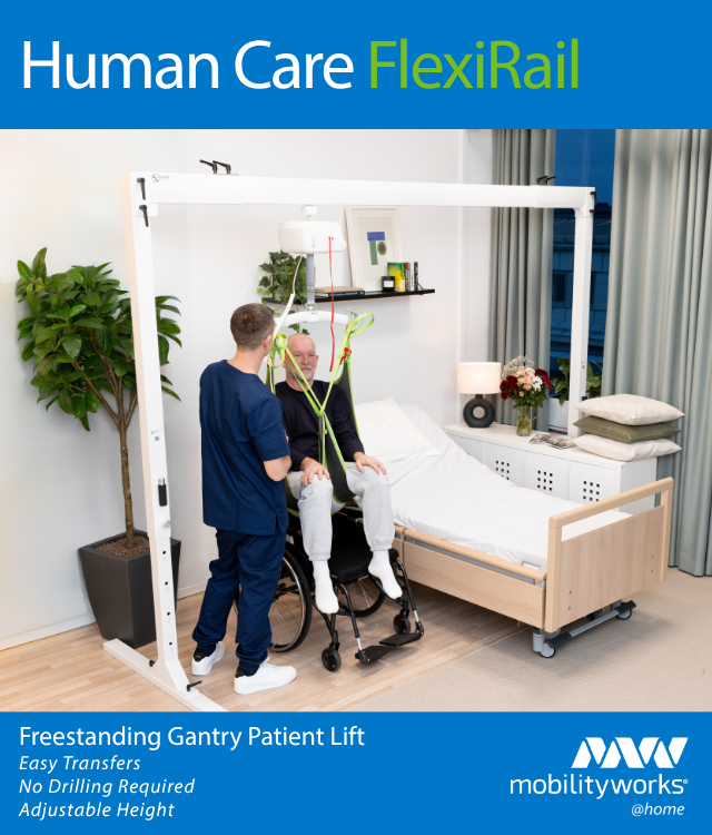 A healthcare worker assists a man in a wheelchair using a freestanding gantry patient lift system next to a hospital bed in a modern room.