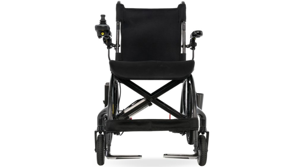 Front view of a black Jazzy Carbon 27X Power Wheelchair featuring joystick controls on both armrests, lowered footrests, and visible small wheels.
