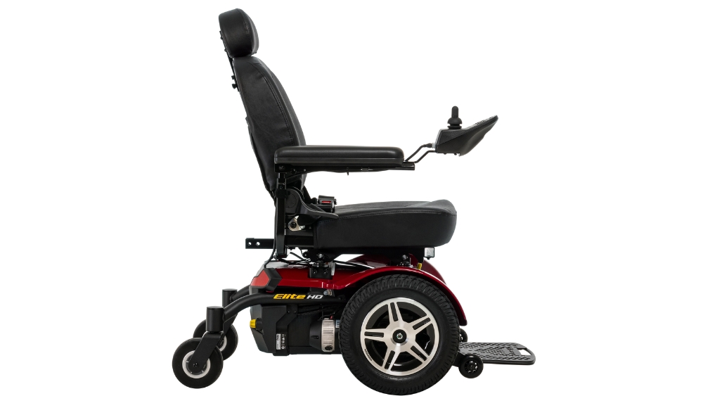 A side view of a Jazzy Elite HD Power Wheelchair featuring a black seat, armrests, joystick control, headrest, and footplate on a red and black wheeled base.