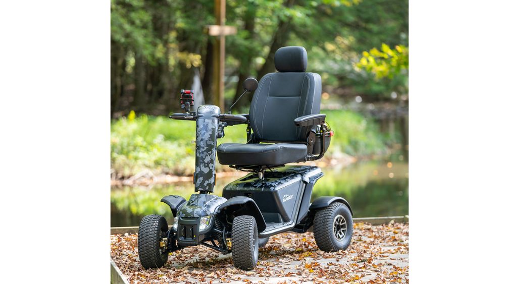 A Baja™ Wrangler® 2 4-Wheel Scooter with armrests and a headrest is parked on a leafy path near trees and water.