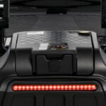 Close-up view of a black electric scooter deck with a textured surface, Lithium Battery for Go Go Carbon compartment, and a horizontal red LED light strip.