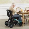 An older man sits in an Ally Power Wheelchair at a dining table, enjoying a meal with orange juice, bread, and fruit.