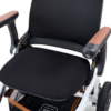 Close-up of the Ally Power Wheelchairs black and white seat with brown armrests, highlighting the cushion, armrest controls, and a portion of a wheel.