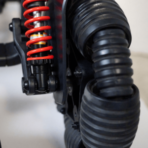 Close-up of a red coil spring shock absorber and large ribbed black tires on an Ally Pro Power Wheelchair.