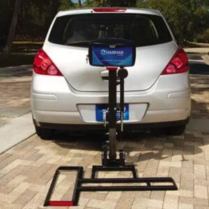 A silver car is parked on a brick driveway with a Harmar Profile Micro Scooter Lift (AL015) securely attached to the back.
