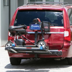 The Harmar Heavy Duty Fusion Lift (AL300HD) secures a mobility scooter on a hitch-mounted carrier attached to the back of a red minivan parked in a paved driveway.