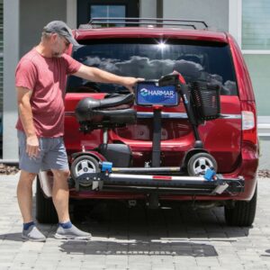 A man stands beside a red SUV equipped with the Harmar Heavy Duty Fusion Lift (AL300HD), which is securely mounted on the rear and effortlessly carries his mobility scooter.