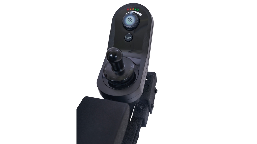 Close-up of a black joystick controller, compatible with the Compass HD Power Wheelchair, showing power and speed adjustment buttons, LED indicator lights, and part of the armrest against a white background.