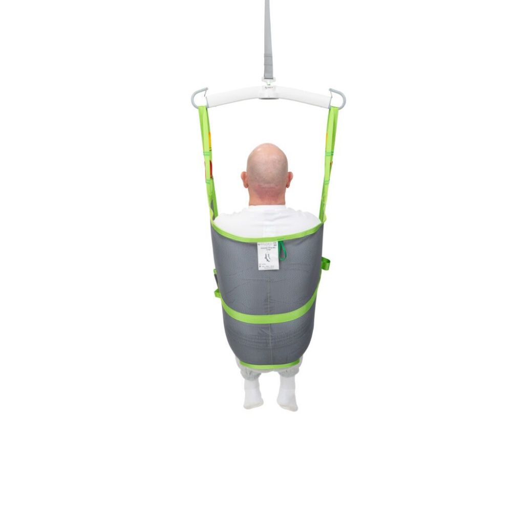 A person sitting in a gray and green Human Care Amputee Sling suspended from a ceiling lift, viewed from behind against a white background.