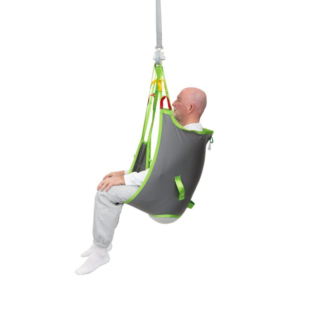 A bald man wearing grey and white clothing sits in a grey and green Human Care Basic Sling attached to an overhead lift system.