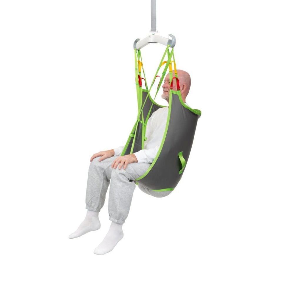 An elderly man sits in a gray and green Human Care Basic Sling, suspended in the air, used for patient transfer or mobility assistance.