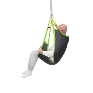 A person in gray pants and white socks sits in a Human Care Comfort Sling, attached to a ceiling lift system, facing away from the camera against a white background.