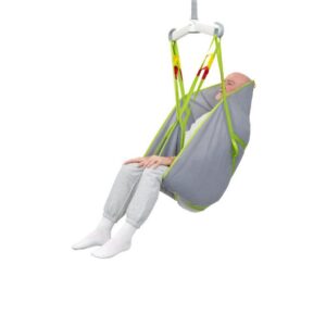 An older adult in gray pants and white socks sits comfortably in a Human Care General Purpose Sling, supported by a gray and green patient lift sling and suspended by a ceiling lift system against a white background.