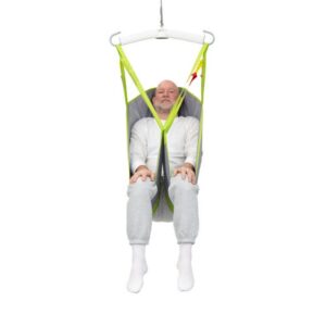 A man in white clothing sits in a green and gray Human Care General Purpose Sling, suspended from a white overhead hoist against a plain white background.