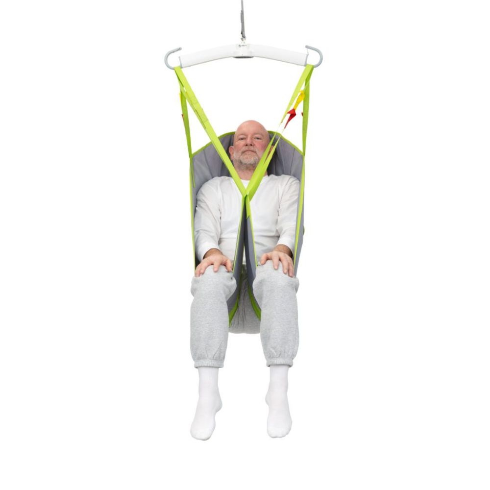 A man in white clothing sits in a green and gray Human Care General Purpose Sling, suspended from a white overhead hoist against a plain white background.