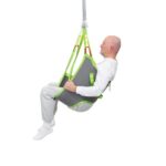 An older man sits in a gray and green Human Care Low Basic Sling, suspended from a ceiling lift, against a white background.